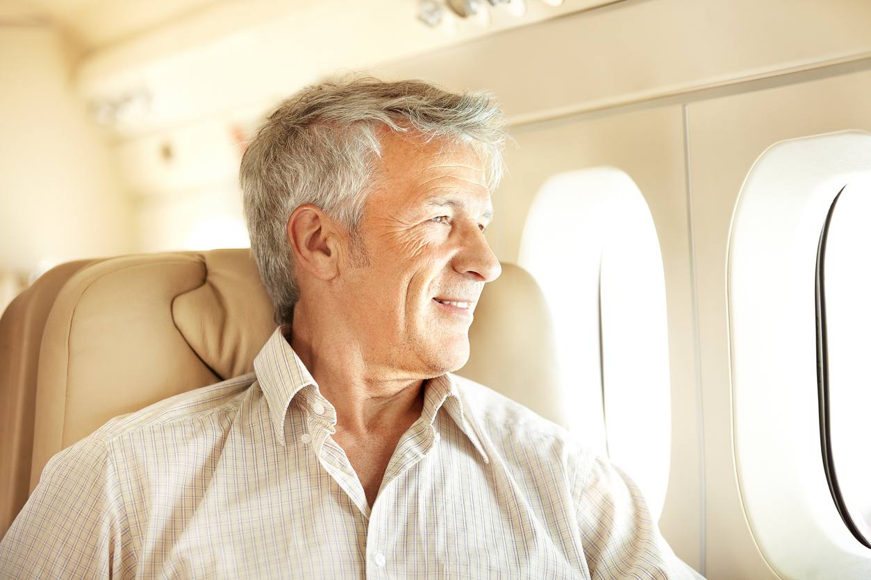 Handsome senior man sitting in an airplane with a smile and looking out the window enjoying In-flight Entertainment systems