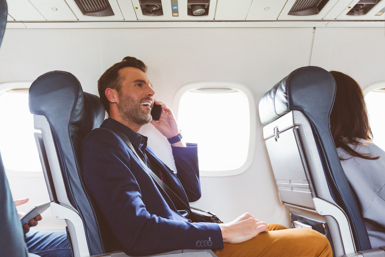 Businessman Talking On Phone while using in-flight Entertainment systems In Plane | AdonisOne